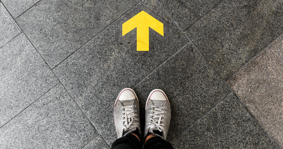 Photo of feet in shoes standing next to an arrow on the floor